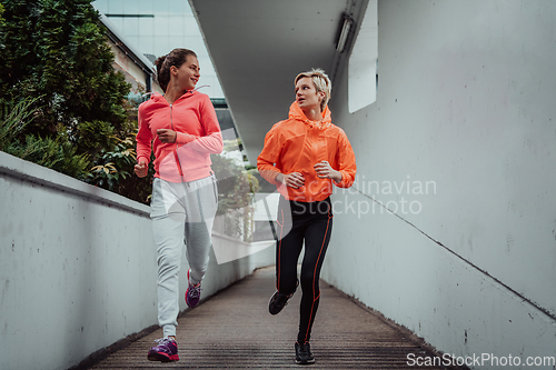 Image of Two women in sports clothes running in a modern urban environment. The concept of a sporty and healthy lifestyle