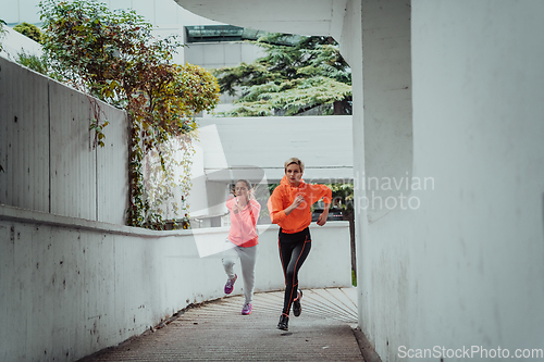 Image of Two women in sports clothes running in a modern urban environment. The concept of a sporty and healthy lifestyle