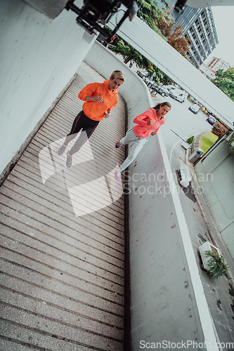 Image of Two women in sports clothes running in a modern urban environment. The concept of a sporty and healthy lifestyle