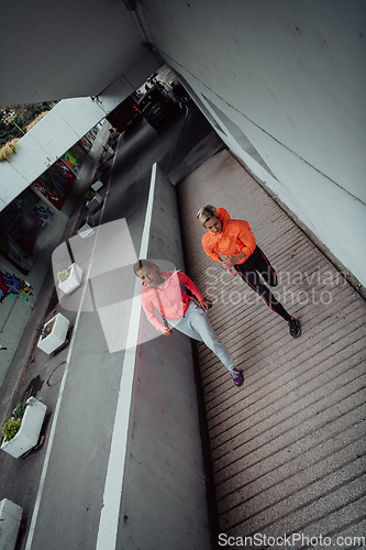 Image of Two women in sports clothes running in a modern urban environment. The concept of a sporty and healthy lifestyle