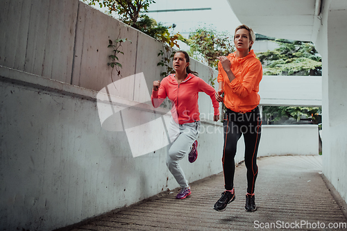 Image of Two women in sports clothes running in a modern urban environment. The concept of a sporty and healthy lifestyle