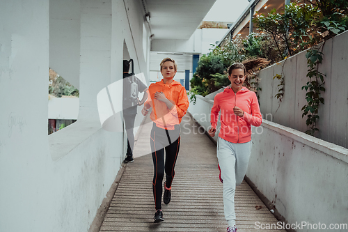 Image of Two women in sports clothes running in a modern urban environment. The concept of a sporty and healthy lifestyle