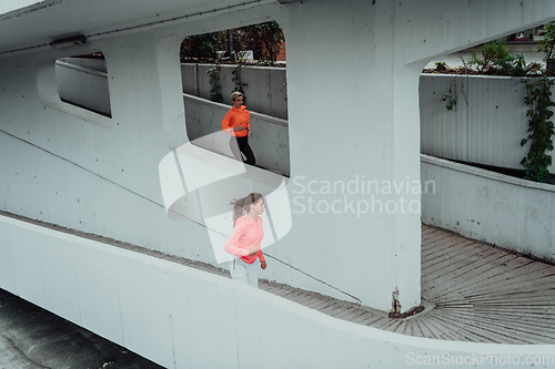 Image of Two women in sports clothes running in a modern urban environment. The concept of a sporty and healthy lifestyle