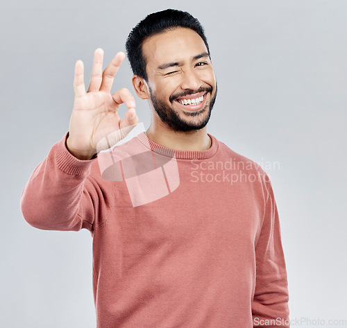 Image of Perfect, winking and portrait of an Asian man with a hand gesture isolated on a white background in studio. Ok, review and a flirty guy with a wink and emoji sign for satisfaction and happiness