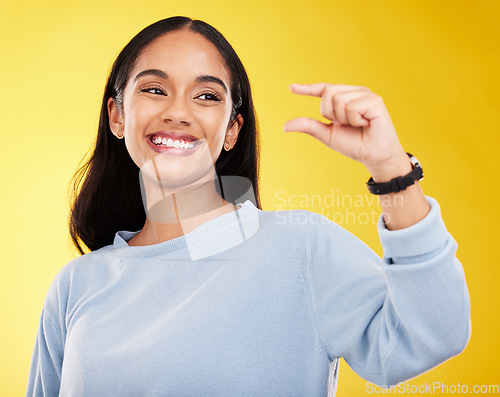 Image of Hand gesture, pinch and measure with a woman on a yellow background in studio to show a size. Smile, review and icon or symbol with an attractive young female posing on a color wall for growth