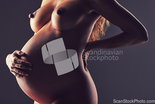 Image of Pregnancy, naked woman in studio with hand on stomach and aesthetic dark background at maternity reveal. Creative photoshoot, art and nude pregnant mother holding belly with healthy body and wellness