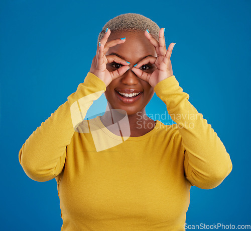 Image of Black woman, binocular hands and eyes in studio portrait for comic funny face with smile, fashion and happy. Student girl, model and ok hand gesture with happiness, youth and pride by blue background