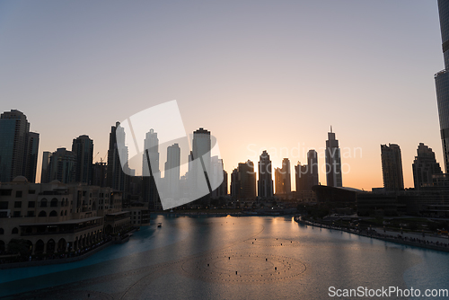 Image of Dubai singing fountains at night lake view between skyscrapers. City skyline in dusk modern architecture in UAE capital downtown.