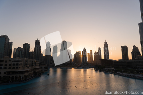 Image of Dubai singing fountains at night lake view between skyscrapers. City skyline in dusk modern architecture in UAE capital downtown.