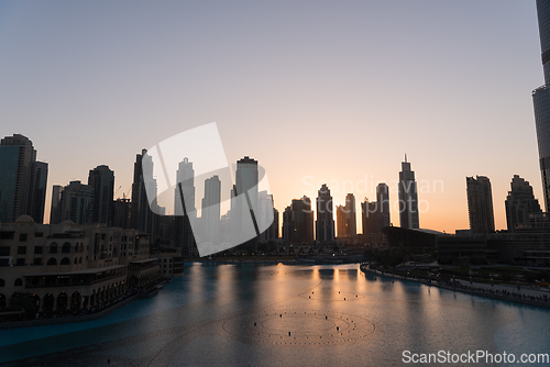 Image of Dubai singing fountains at night lake view between skyscrapers. City skyline in dusk modern architecture in UAE capital downtown.