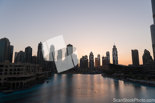 Image of Dubai singing fountains at night lake view between skyscrapers. City skyline in dusk modern architecture in UAE capital downtown.