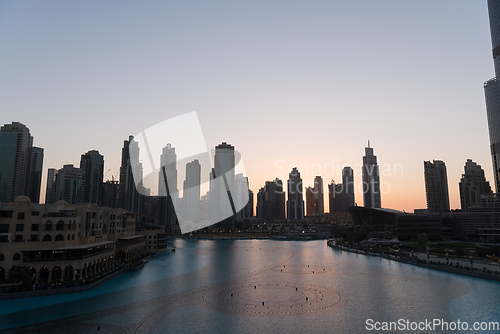 Image of Dubai singing fountains at night lake view between skyscrapers. City skyline in dusk modern architecture in UAE capital downtown.