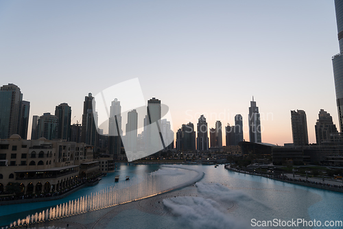 Image of Dubai singing fountains at night lake view between skyscrapers. City skyline in dusk modern architecture in UAE capital downtown.