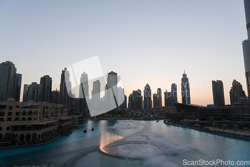 Image of Dubai singing fountains at night lake view between skyscrapers. City skyline in dusk modern architecture in UAE capital downtown.