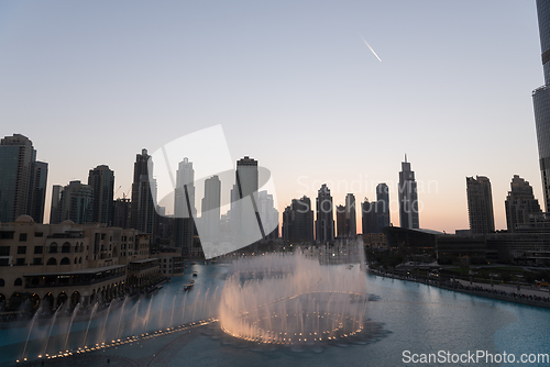 Image of Dubai singing fountains at night lake view between skyscrapers. City skyline in dusk modern architecture in UAE capital downtown.