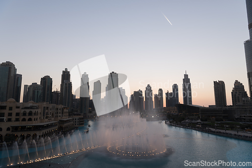 Image of Dubai singing fountains at night lake view between skyscrapers. City skyline in dusk modern architecture in UAE capital downtown.