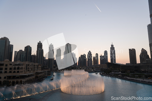 Image of Dubai singing fountains at night lake view between skyscrapers. City skyline in dusk modern architecture in UAE capital downtown.