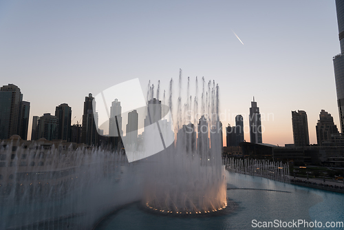 Image of Dubai singing fountains at night lake view between skyscrapers. City skyline in dusk modern architecture in UAE capital downtown.