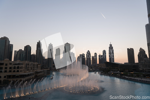 Image of Dubai singing fountains at night lake view between skyscrapers. City skyline in dusk modern architecture in UAE capital downtown.