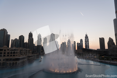 Image of Dubai singing fountains at night lake view between skyscrapers. City skyline in dusk modern architecture in UAE capital downtown.