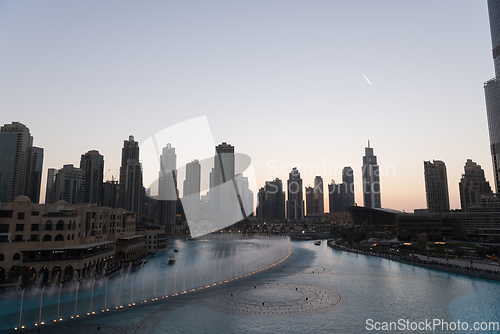 Image of Dubai singing fountains at night lake view between skyscrapers. City skyline in dusk modern architecture in UAE capital downtown.