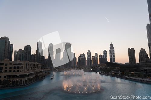 Image of Dubai singing fountains at night lake view between skyscrapers. City skyline in dusk modern architecture in UAE capital downtown.