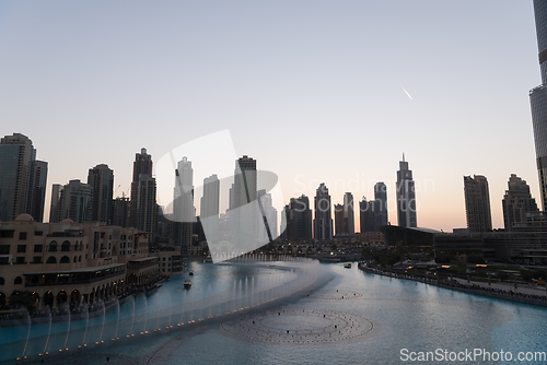 Image of Dubai singing fountains at night lake view between skyscrapers. City skyline in dusk modern architecture in UAE capital downtown.