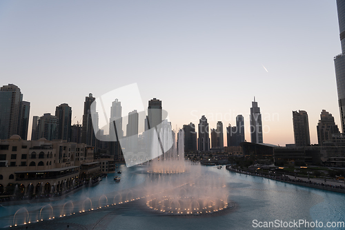 Image of Dubai singing fountains at night lake view between skyscrapers. City skyline in dusk modern architecture in UAE capital downtown.