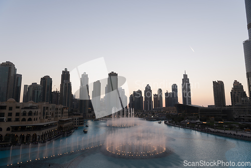 Image of Dubai singing fountains at night lake view between skyscrapers. City skyline in dusk modern architecture in UAE capital downtown.