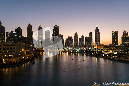 Image of Dubai singing fountains at night lake view between skyscrapers. City skyline in dusk modern architecture in UAE capital downtown.