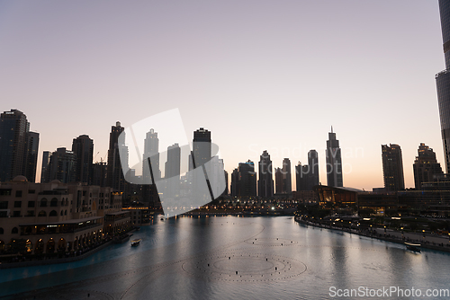 Image of Dubai singing fountains at night lake view between skyscrapers. City skyline in dusk modern architecture in UAE capital downtown.