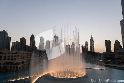 Image of Dubai singing fountains at night lake view between skyscrapers. City skyline in dusk modern architecture in UAE capital downtown.