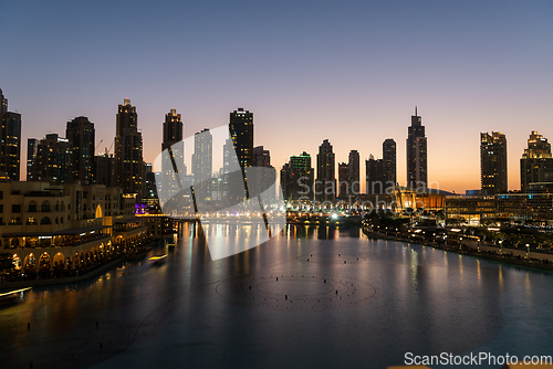 Image of Dubai singing fountains at night lake view between skyscrapers. City skyline in dusk modern architecture in UAE capital downtown.