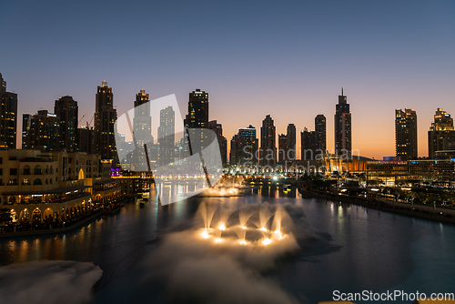 Image of Dubai singing fountains at night lake view between skyscrapers. City skyline in dusk modern architecture in UAE capital downtown.