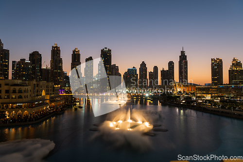 Image of Dubai singing fountains at night lake view between skyscrapers. City skyline in dusk modern architecture in UAE capital downtown.