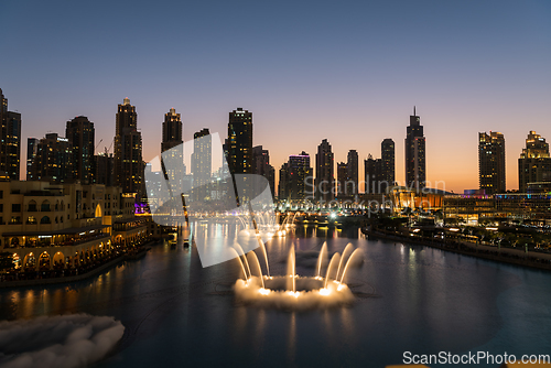 Image of Dubai singing fountains at night lake view between skyscrapers. City skyline in dusk modern architecture in UAE capital downtown.