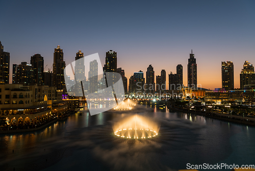 Image of Dubai singing fountains at night lake view between skyscrapers. City skyline in dusk modern architecture in UAE capital downtown.