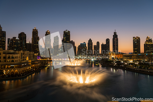 Image of Dubai singing fountains at night lake view between skyscrapers. City skyline in dusk modern architecture in UAE capital downtown.