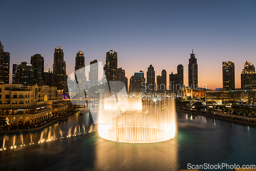 Image of Dubai singing fountains at night lake view between skyscrapers. City skyline in dusk modern architecture in UAE capital downtown.