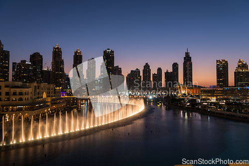 Image of Dubai singing fountains at night lake view between skyscrapers. City skyline in dusk modern architecture in UAE capital downtown.