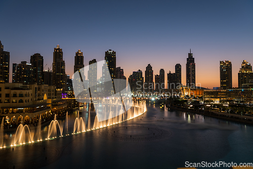 Image of Dubai singing fountains at night lake view between skyscrapers. City skyline in dusk modern architecture in UAE capital downtown.
