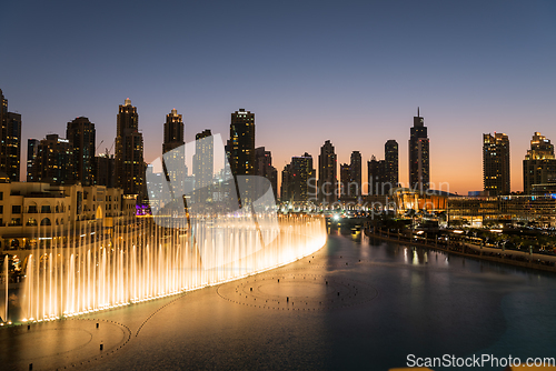 Image of Dubai singing fountains at night lake view between skyscrapers. City skyline in dusk modern architecture in UAE capital downtown.