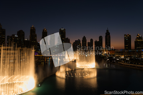 Image of Dubai singing fountains at night lake view between skyscrapers. City skyline in dusk modern architecture in UAE capital downtown.