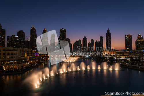 Image of Dubai singing fountains at night lake view between skyscrapers. City skyline in dusk modern architecture in UAE capital downtown.