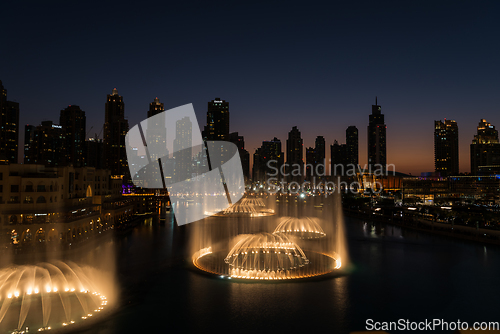 Image of Dubai singing fountains at night lake view between skyscrapers. City skyline in dusk modern architecture in UAE capital downtown.