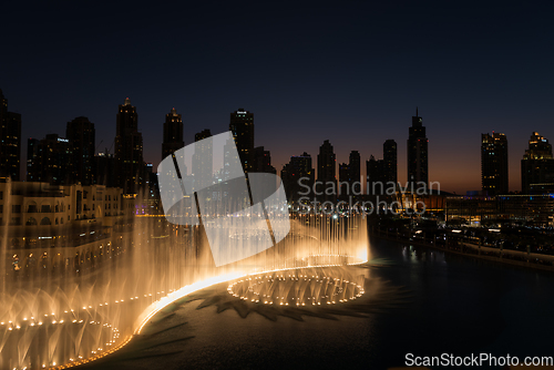 Image of Dubai singing fountains at night lake view between skyscrapers. City skyline in dusk modern architecture in UAE capital downtown.