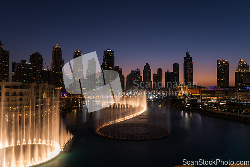 Image of Dubai singing fountains at night lake view between skyscrapers. City skyline in dusk modern architecture in UAE capital downtown.