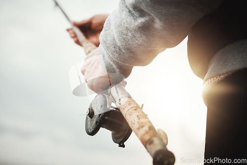 Image of Hands, fishing and rod with a man in nature, enjoying a weekend trip his hobby or pastime at sunset. Morning, flare and low angle with a male fisherman casting a line outdoor in the wilderness