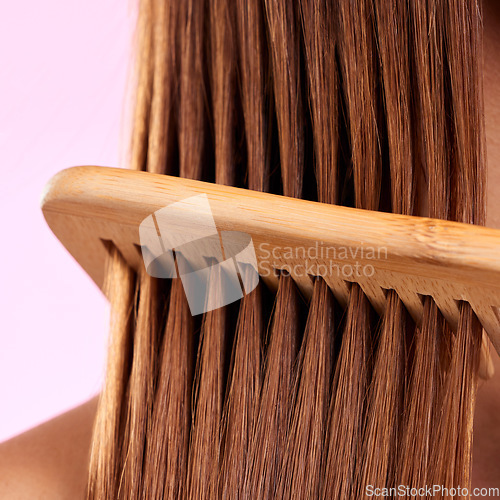 Image of Beauty, comb and wood with hair of woman for health, salon and close up in studio. Wellness, keratin and natural bamboo brush with female model for cosmetics, self care and shine on pink background