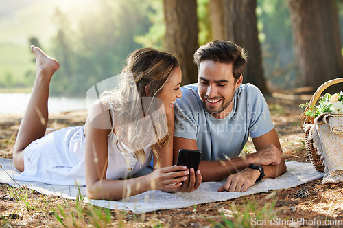 Image of Couple on picnic with smartphone, relax together in nature and social media with travel and bonding outdoor. Happiness, man and woman lying down and scroll internet in forest with smile